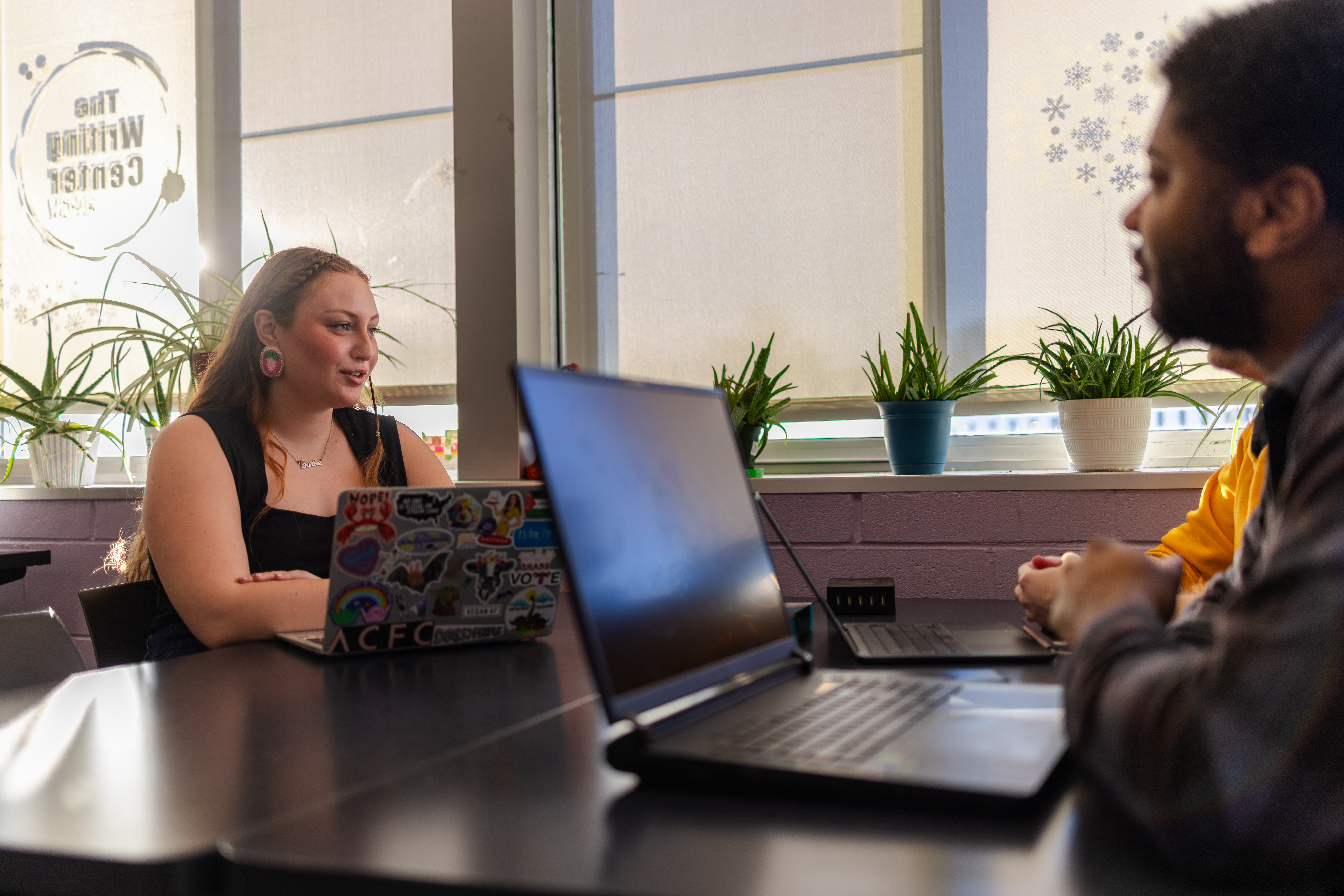 MSU student Kaylin Casper sits at a table in the Writing Center, talking to fellow students with several laptops in front of them.