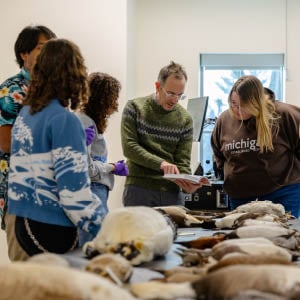 Assistant Professor Matthew Toomey stands at center surrounded by students in his Biology of Birds course taught at the MSU Museum. On the table in front of them is a wide variety of stuffed birds from the museum collections.