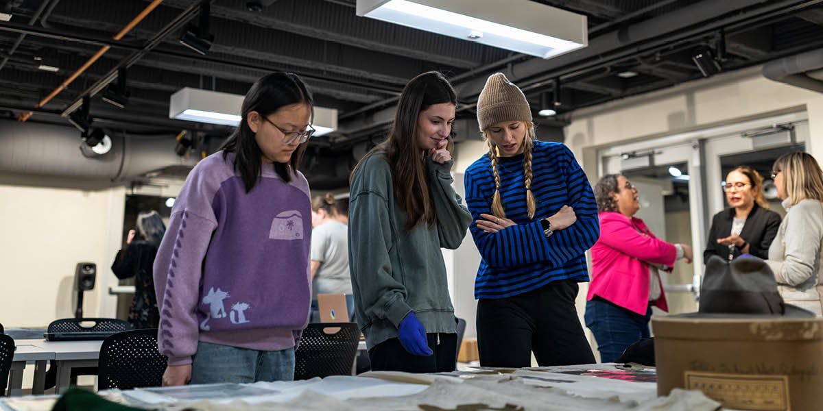 Three students look over items from the Spartan Traditions collection in the Immersive Lab at the MSU Museum.