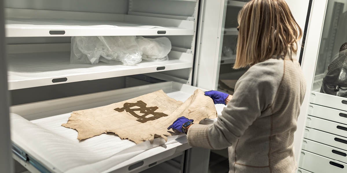 An MSU Museum employee gently places a tattered Michigan College sweater back into a collections display case.