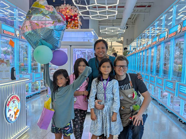 Spartan alums Michal and Agnes Filipowski stand with their three daughters surrounded by claw machines at their Novi-based business, Klawsome.