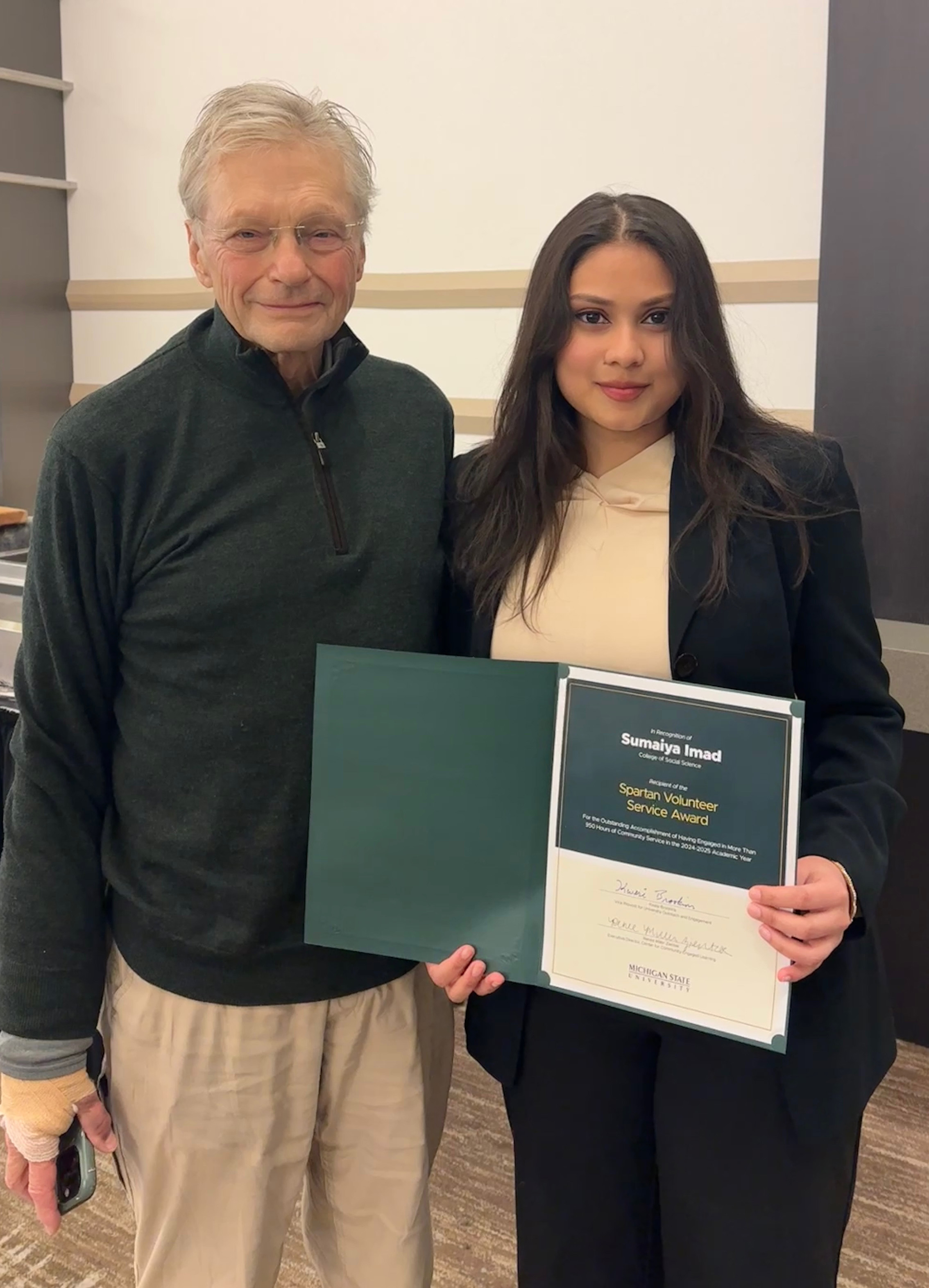 Social Science Scholar Sumaiya Imad holding an award and standing with her Spartan mentor Charles Dobis.