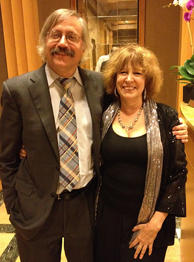 Randy and Phyllis Cowen dressed in formal attire stand arm in arm, smiling for a photo at an indoor event.
