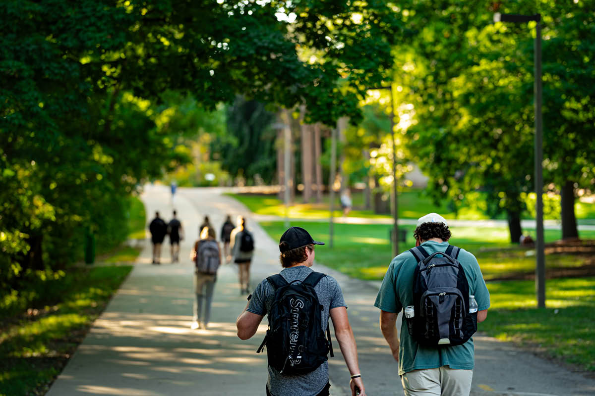 Michigan State students walk along a tree-lined campus pathway carrying backpacks between classes.