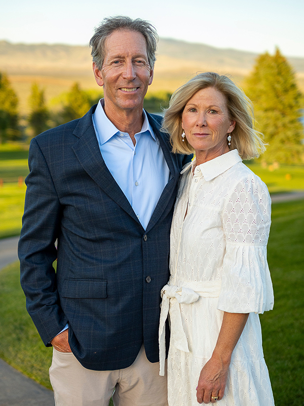 Tom and Anne Wright standing outdoors on a golf course at sunset, smiling at the camera with trees and rolling hills in the background.