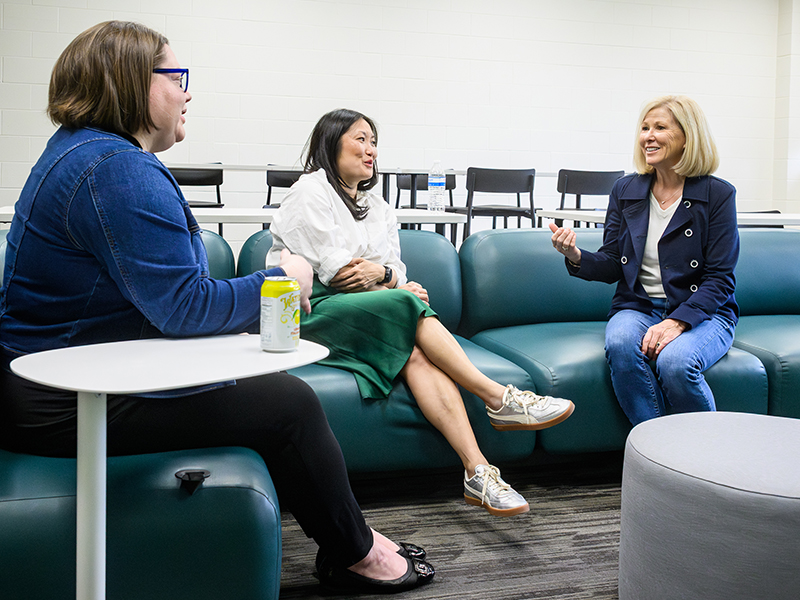 Three women sit together in a lounge area, smiling and talking during a casual conversation on Michigan State University's campus.