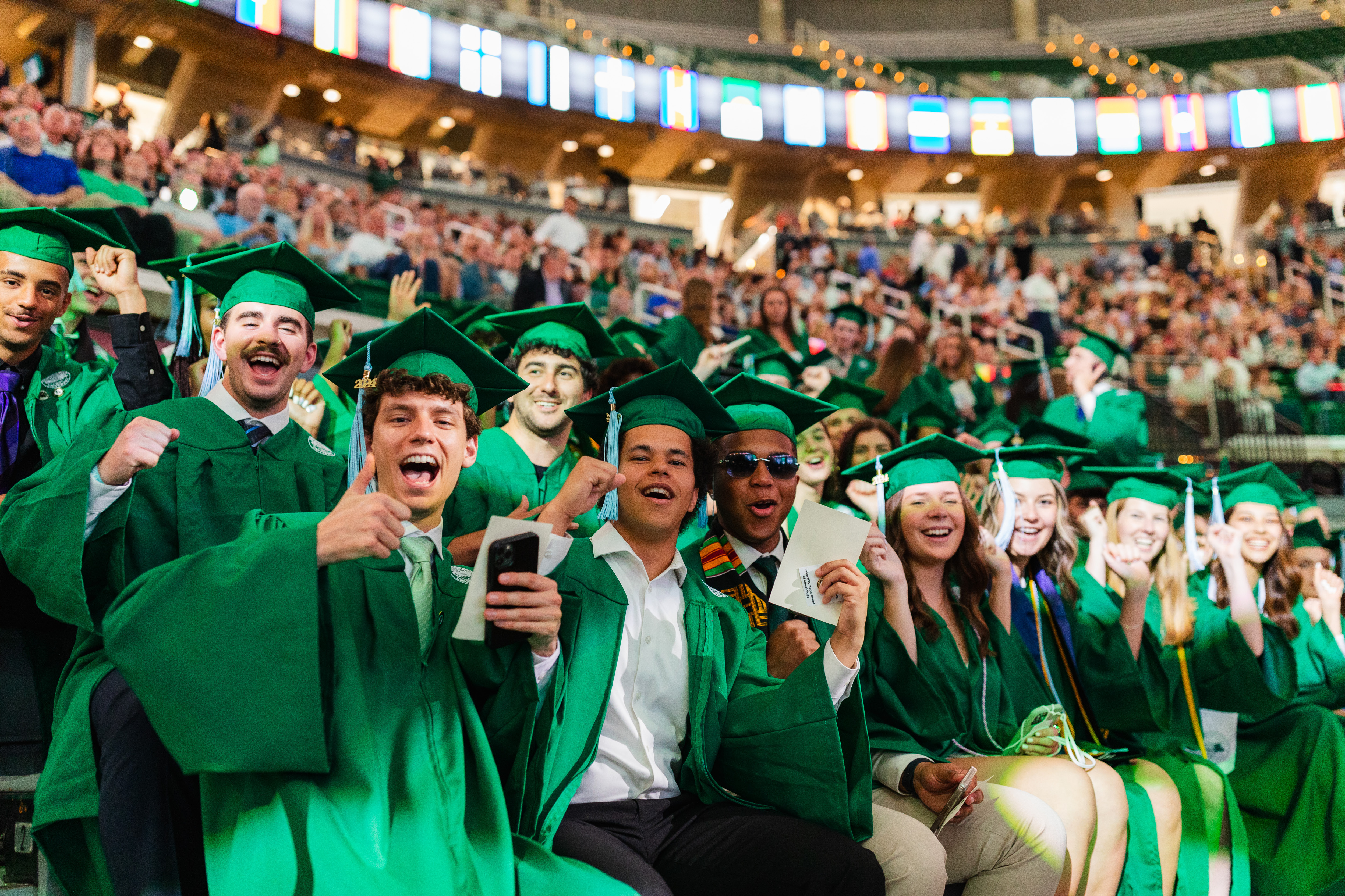 A group of joyful Spartan graduates in caps and gowns at the commencement ceremony in Breslin Center