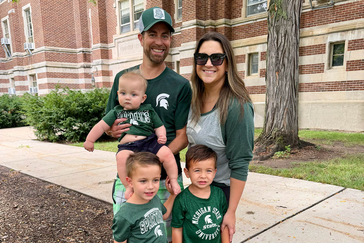 Jeff and Lauren Bearance stand with their three sons on MSU's campus with all of them wearing Spartan gear.