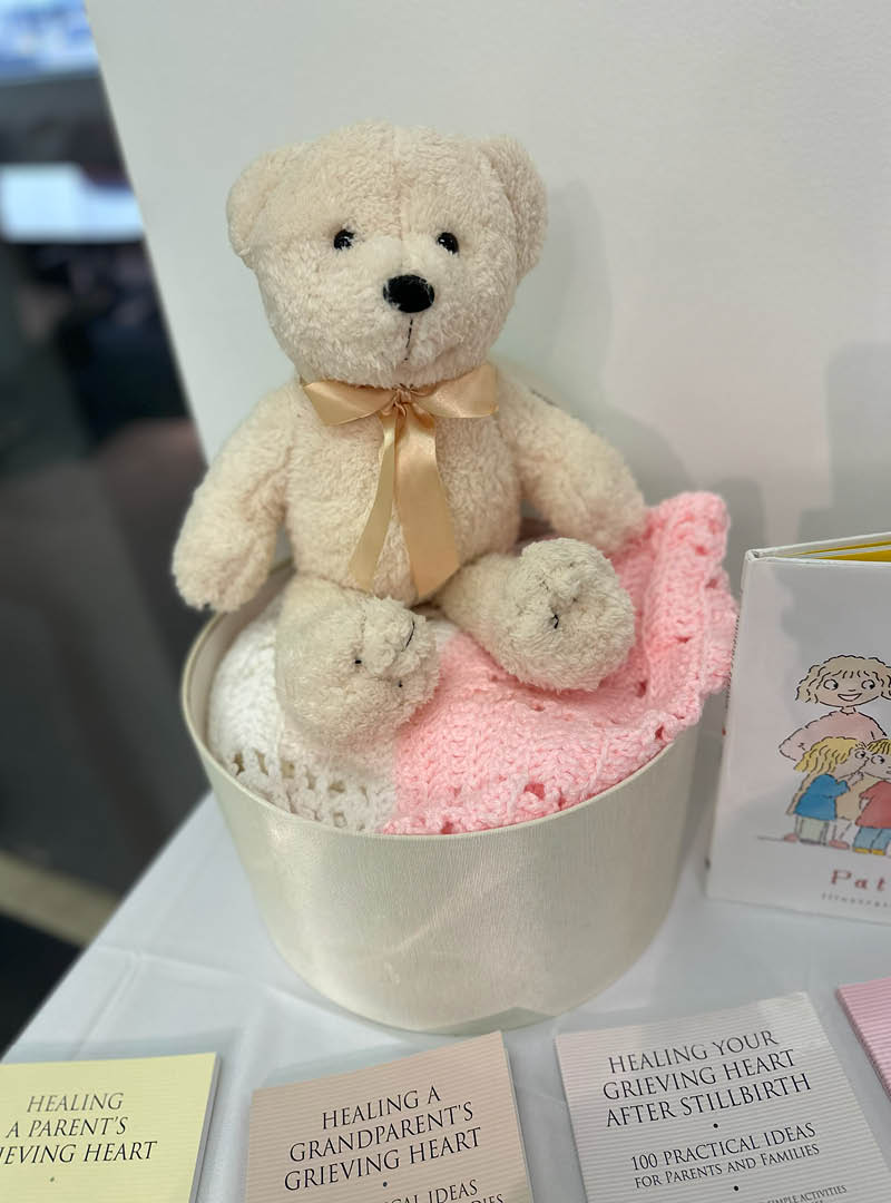 A white teddy bear toy sits atop a box surrounded by packets about grief and loss.