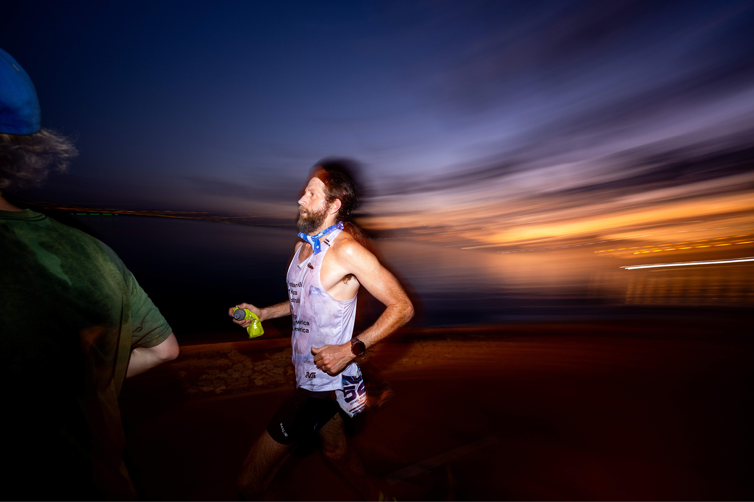 Ultrarunner Mike Wardian running outdoors in the evening with a purple sky above and a sunset in the distance. 