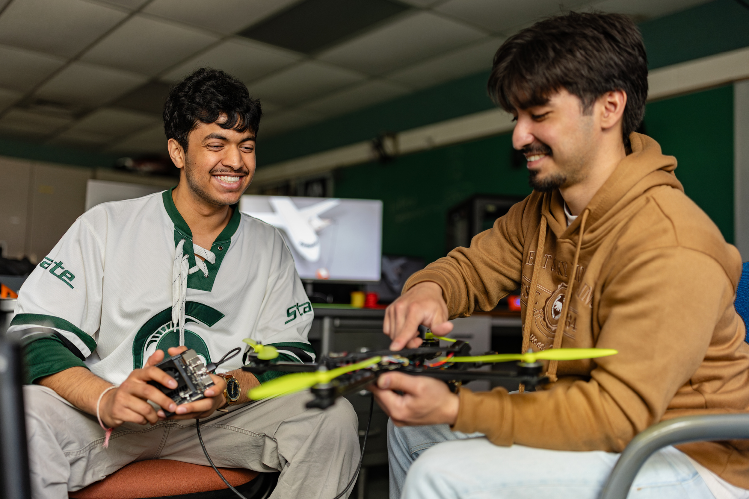 Williams Scholar Tejas Agrawal in a Michigan State University hockey jersey, working alongside a colleague with a drone.