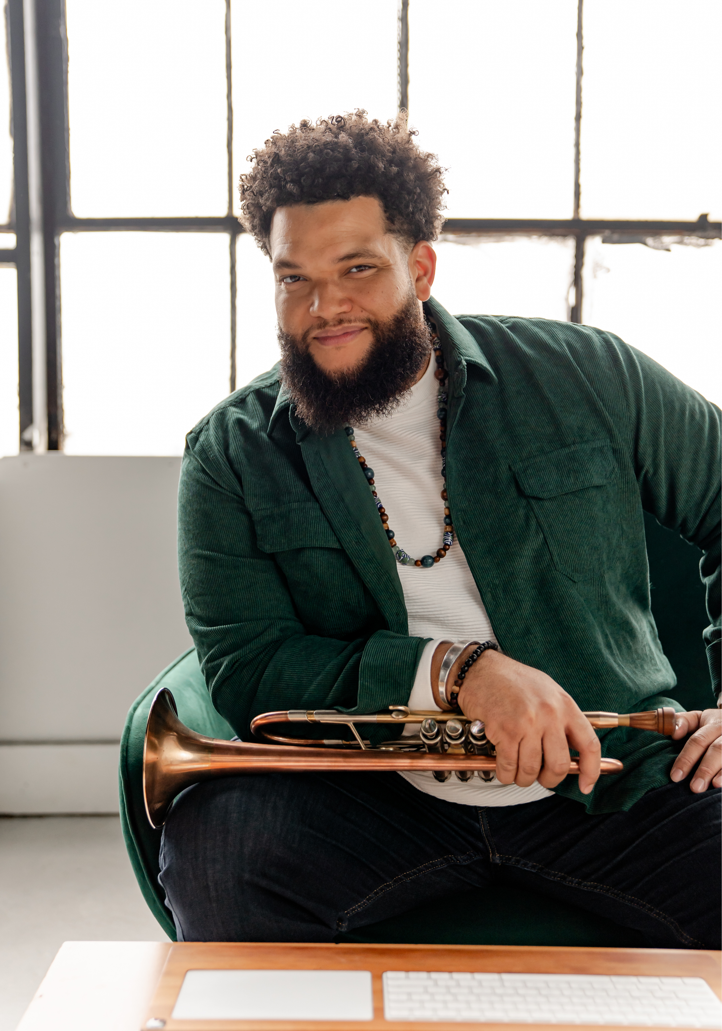 Kris Johnson seated and posed in a bright studio holding his trumpet in his lap.
