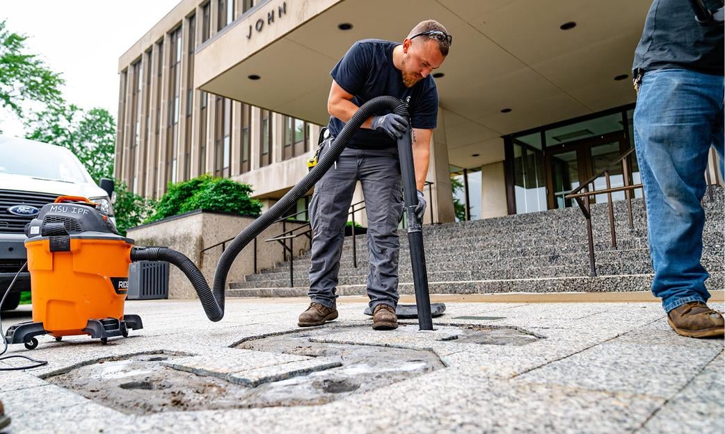 IPF workers replace bronze block "S" in front of Hannah Admin. Building.