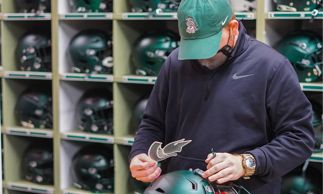 equipment team member places decals on MSU football helmet.