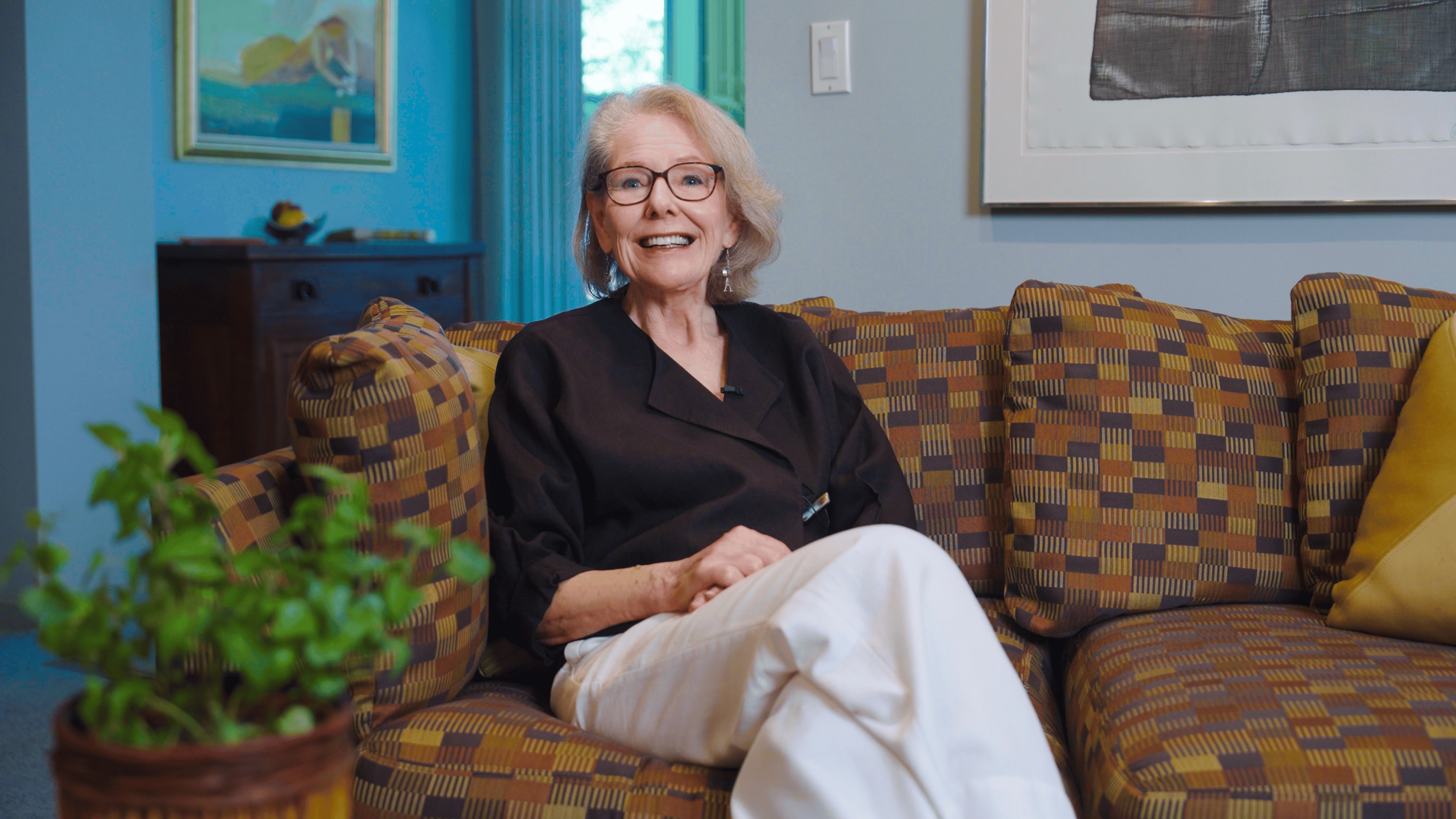 A woman in glasses and brown shirt sits on a patterned sofa