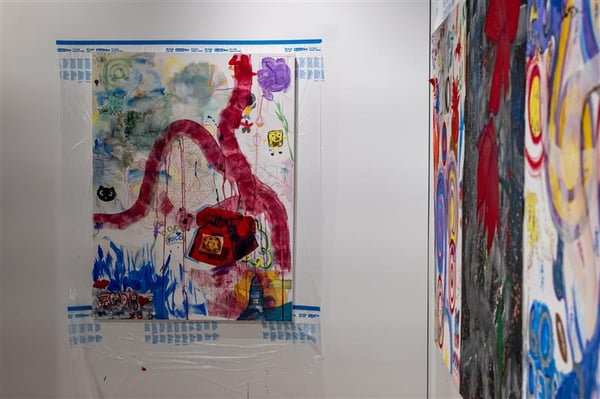 Abstract art placed on white walls. The pieces feature large swaths of red, green and blue paint. 