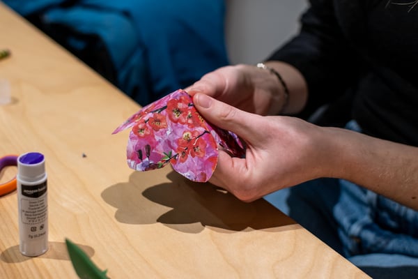 A close up of someone's hands holding pink floral patterned origami paper. The person is in the midst of using both hands to create an upside down flower shape.