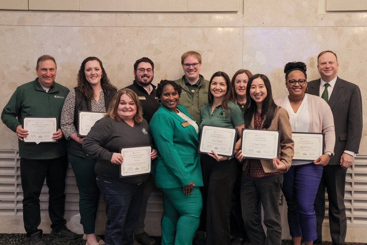 Award recipients hold their certificates while stand smiling together, along with Mark Largent and Ebony Green.