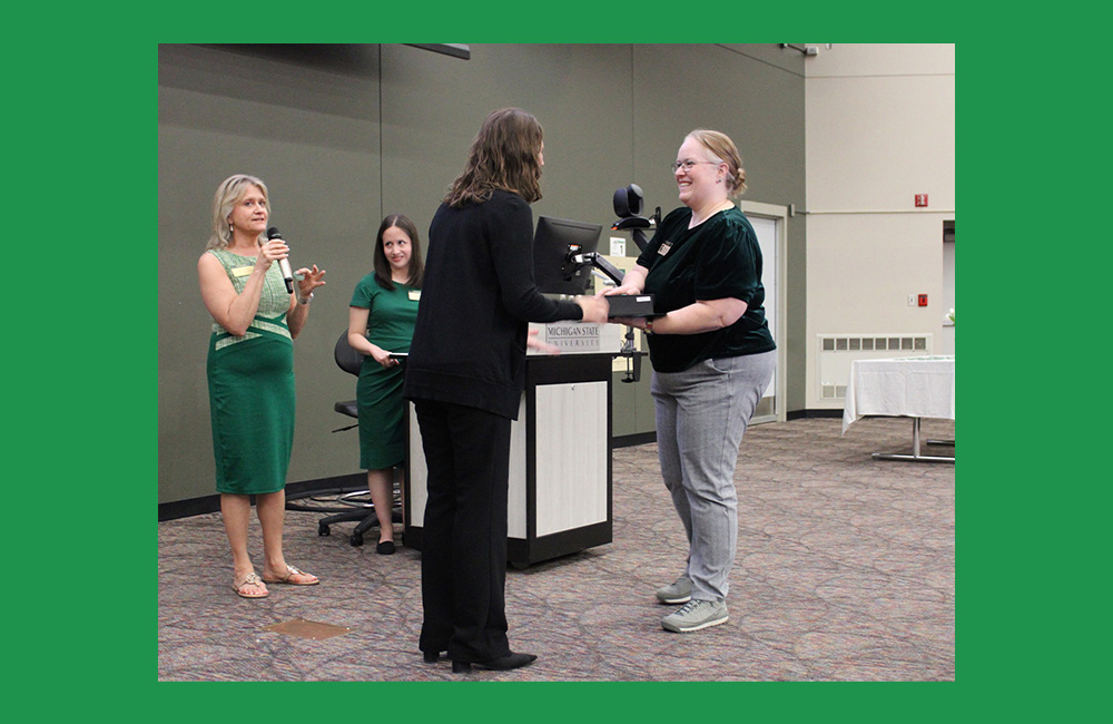 People standing near a podium. A person in the center is leaning forward to shake another person's hand. 