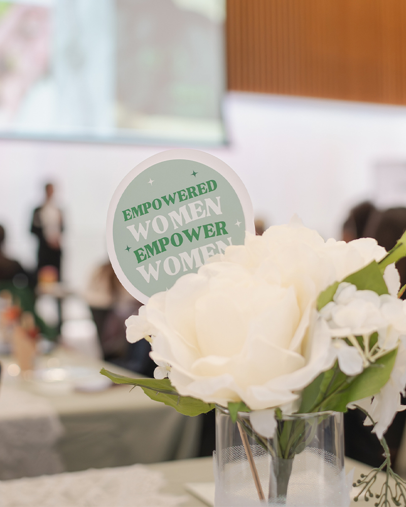 Close up of a white rose flower in a vase with a small sign next to it reading 