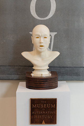 A marbled head is on display on a wooden block, placed above a sign in the MSU Museum that reads