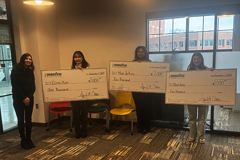 Four individuals stand indoors holding large scholarship checks from MSU Federal Credit Union. From left to right, three recipients hold checks made out to Eileen Kim for $1,000, Misa Jeffries for $2,000, and Olivia Booker for $500. 