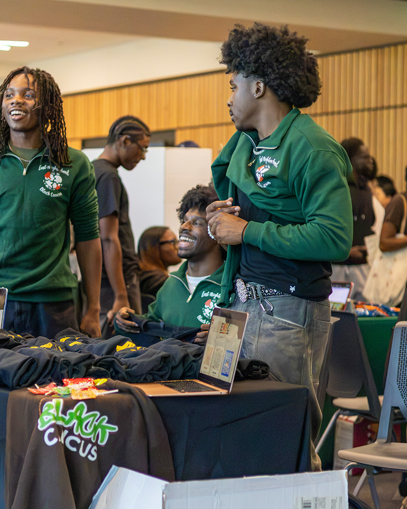 Students staff a Black Caucus organization table at a campus involvement fair, displaying apparel and informational materials.