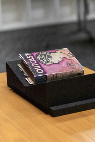 A copy of Outcast rests on a wooden display stand on a table.