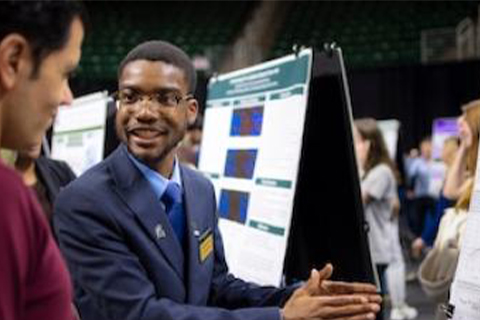 Student researcher shares a research poster with an attendee during an undergraduate research showcase.