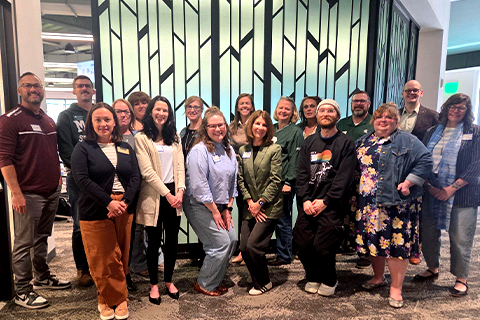 Group of staff members standing together in front of a decorative geometric wall inside a conference or office building.
