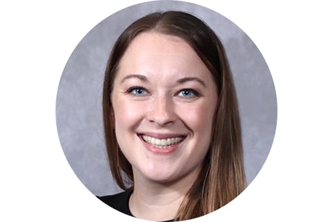 Portrait. Subject is looking at the camera and smiling against a grey back drop, with long blonde hair. 
