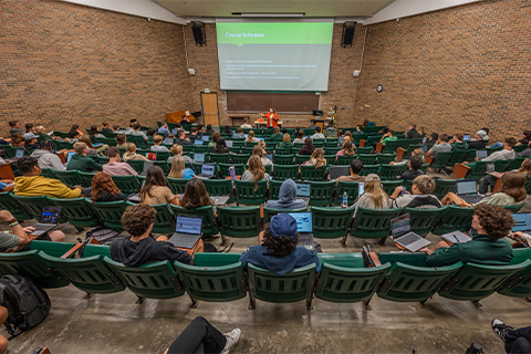 Michigan State University students sit in a large lecture hall in green chairs facing an instructor and a screen during the first day of classes for the Fall 2023 semester at the East Lansing campus.