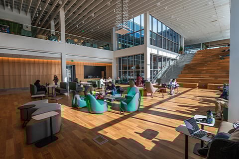 Interior view of MSU's Multicultural Center. In focus is a large set of wooden stairs and a sitting/working area featuring green and grey plush seats and couches and tables.