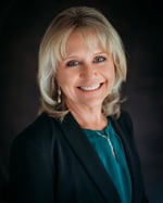 Studio portrait of Amy Martin wearing a dark blazer over a green top. She has short blond hair. 