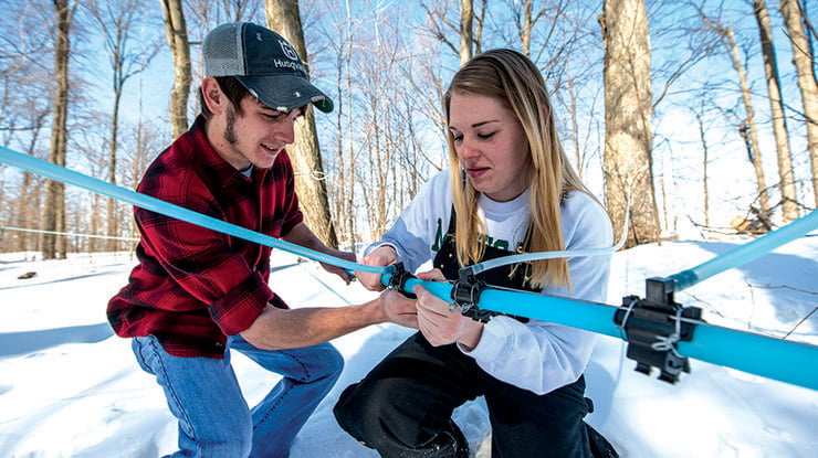 Students working toward a forestry degree assemble forestry equipment outdoors on a bright, snowy day.
