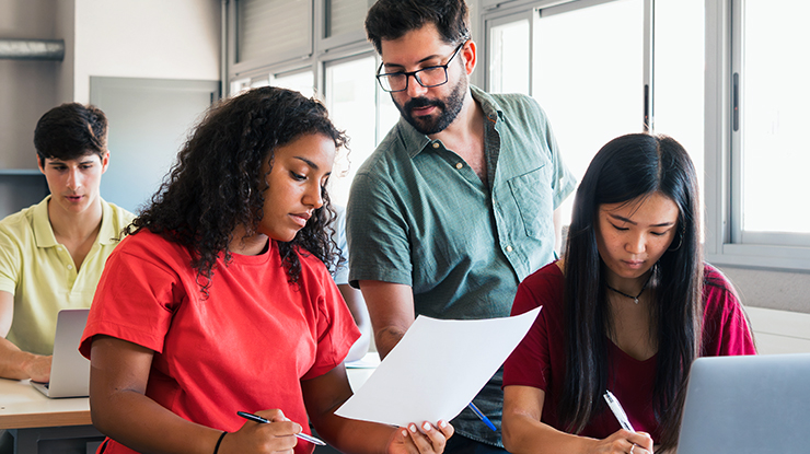 Professor assisting a diverse group of students reviewing coursework in a classroom as part of Michigan State University's Spanish education degree program.