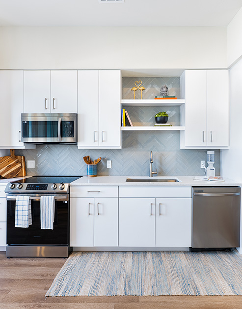 Modern open gourmet kitchen built into the wall with white cabinets, stainless steel appliances on wood floors at MAA Breakwater luxury apartments in Tampa, FL