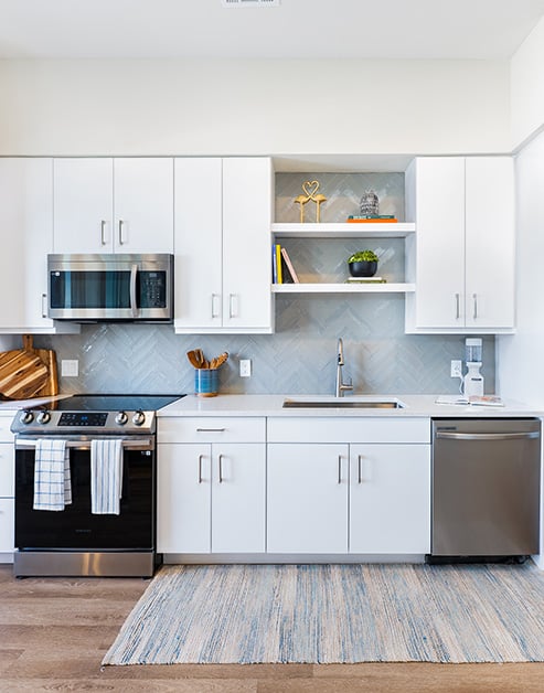 Modern open gourmet kitchen built into the wall with white cabinets, stainless steel appliances on wood floors at MAA Breakwater luxury apartments in Tampa, FL