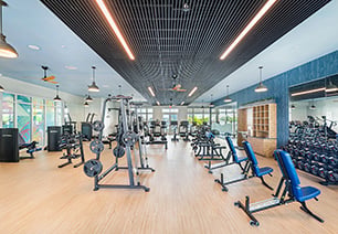 Wide view of state-of-the-art fitness center with wood beam ceiling, weight machines and benches, free weight racks and hanging light fixtures on wood floors at MAA Breakwater luxury apartments in Tampa, FL
