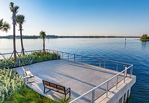Waterfront spacious outdoor deck with sitting benches surrounded by lush greenery and palm trees with a bay view at MAA Breakwater luxury apartments in Tampa, FL