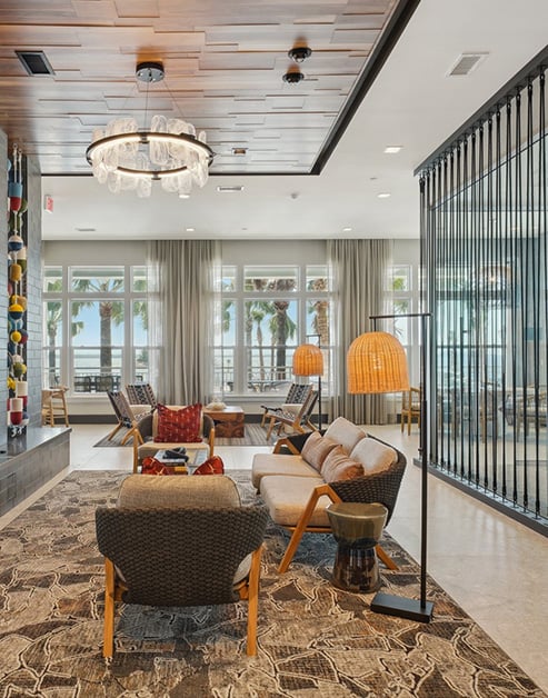 Upscale clubhouse with chandelier, sitting areas with area rugs next to large picture windows of waterfront views at MAA Breakwater luxury apartments in Tampa, FL