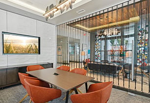 Modern clubhouse conference room with stylish rope-style wall divider, conference table with orange chairs next to a wall-mounted TV at MAA Breakwater luxury apartments in Tampa, FL