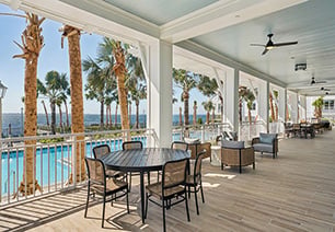 Poolside veranda on wood floors with multiple sitting areas, ceiling fans with white columns and guardrails next to palm trees at MAA Breakwater luxury apartments in Tampa, FL