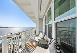 Outdoor patio with cushioned chairs and round side table with white guardrails with a waterfront view at MAA Breakwater luxury apartments in Tampa, FL