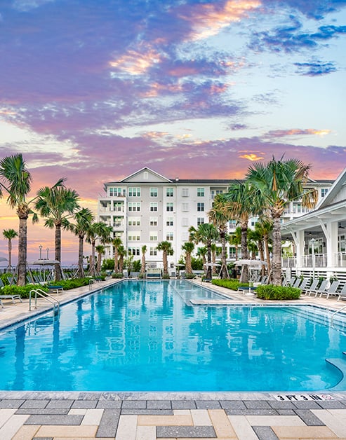 Resort-style swimming pool with metal handrail and palm trees next to the clubhouse with a porch at MAA Breakwater luxury apartments in Tampa, FL