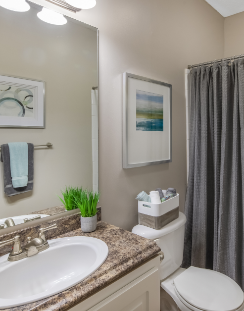 Modern bathroom with a single vanity sink and brown marble countertops and bathtub with grey shower curtains at MAA Barrett Creek luxury apartments in Marietta, GA