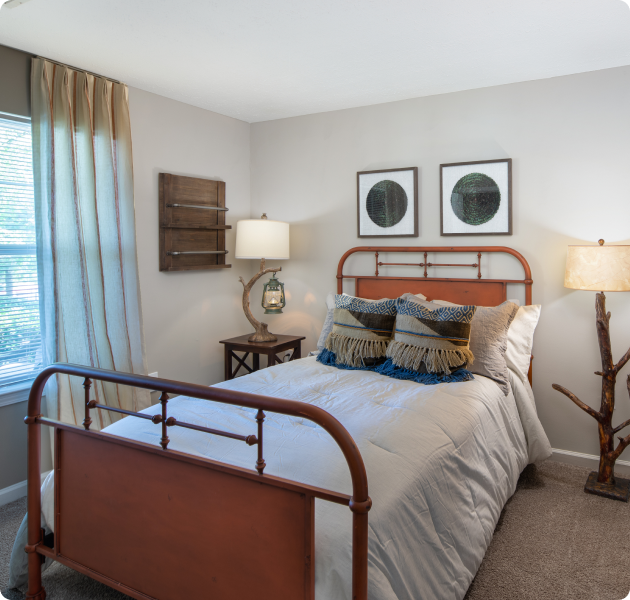 Model guest bedroom with rustic décor and a window with curtains at MAA Berkeley Lake luxury apartments in Duluth, GA