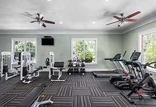 Side view of fitness center with ceiling fans, weight machines, a wall-mounted TV and picture windows at MAA Berkeley Lake luxury apartments in Duluth, GA