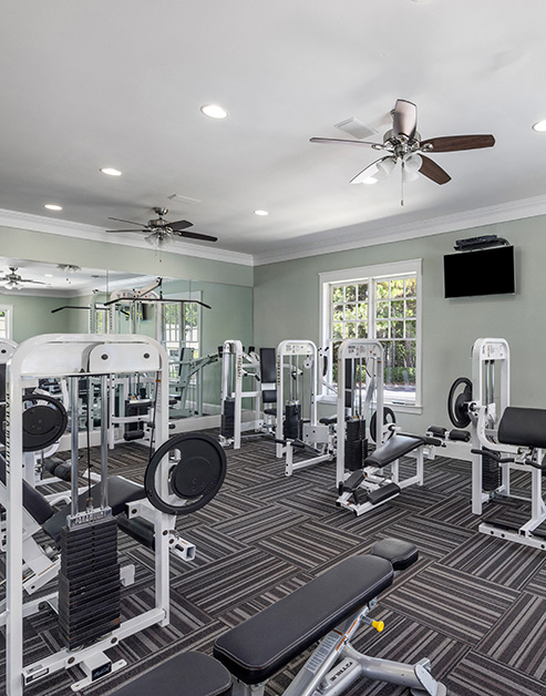 Community fitness center with ceiling fans, weight machines, a wall-mounted TV and picture windows at MAA Berkeley Lake luxury apartments in Duluth, GA