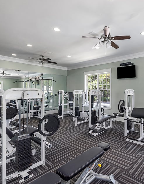 Community fitness center with ceiling fans, weight machines, a wall-mounted TV and picture windows at MAA Berkeley Lake luxury apartments in Duluth, GA
